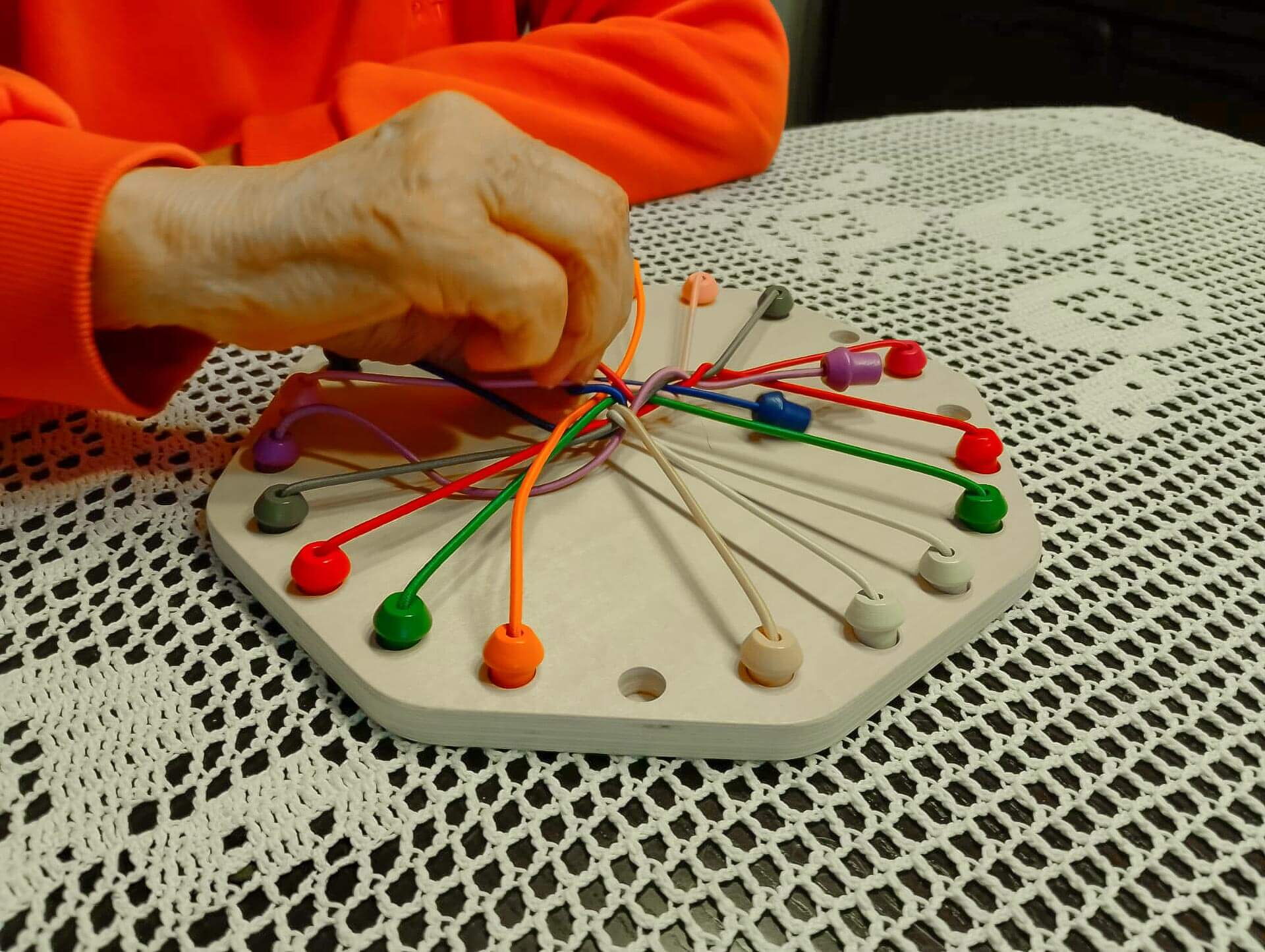 Eine Hand einer Seniorin greift nach bunten Schnüren auf einem Spielbrett, um die kognitive Betreuung bei Demenz zu fördern.
